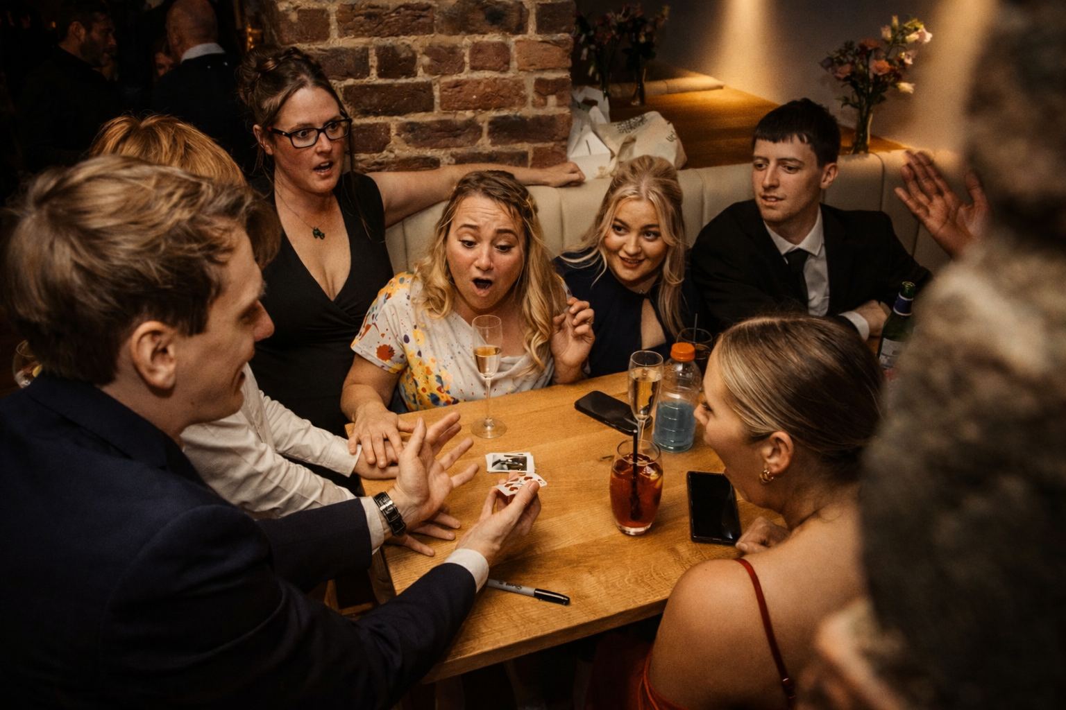 Magician performing close-up magic at a birthday party, guests astonished around a table